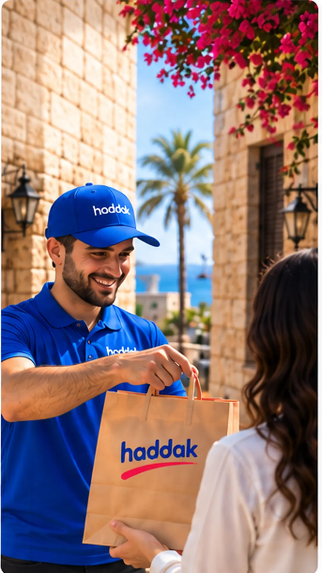 A Haddak rider in a blue cap handing a Haddak bag to a customer at her door on a stone street in Sour.